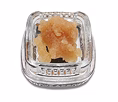 Golden cannabis concentrate in a clear glass jar with textured lid and brand label