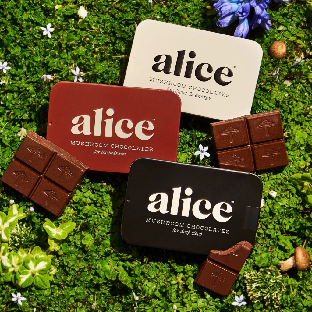 Three tins of Alice mushroom chocolates labeled for focus, sleep, and bedroom, displayed with chocolate squares on a green floral background.